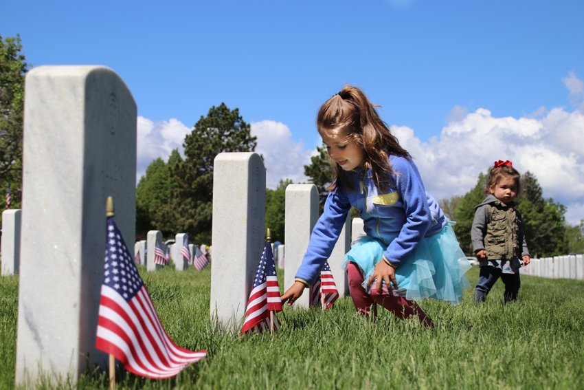 Grace Dauro, 5, lays a rose on a grave at Fort Logan National Cemetery as her sister Vivienne looks on.